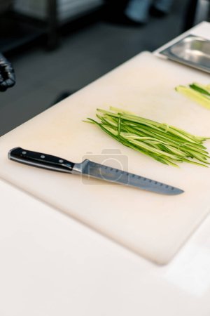 Photo for Close-up of a sushi maker in gloves cutting a cucumber with a professional kitchen knife on white board in a professional kitchen while making sushi - Royalty Free Image