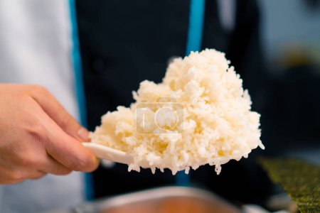 Téléchargez les photos : Gros plan d'un chef sushi prenant du riz avec une cuillère de riz tout en préparant des sushis sur fond d'anguille et de saumon - en image libre de droit