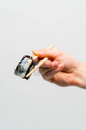 Foto de Primer plano de sushi california con arroz negro y anguila que un hombre sostiene con palillos sobre fondo blanco - Imagen libre de derechos
