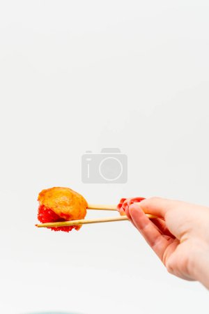 Téléchargez les photos : Gros plan de sushis cuits au four aux crevettes et anguilles tenus avec des baguettes par la main d'un homme sur fond blanc - en image libre de droit