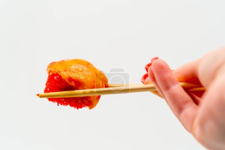 Foto de Primer plano de sushi al horno con camarones y anguila sostenida con palillos por la mano de un hombre sobre fondo blanco - Imagen libre de derechos