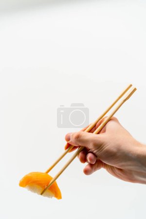 Foto de Primer plano de los palillos de mano de un hombre sosteniendo un sushi de salmón en el aire sobre un fondo blanco - Imagen libre de derechos