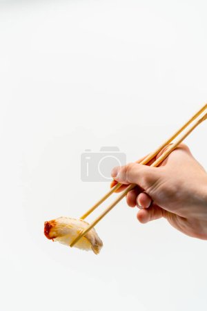 Foto de Primer plano de la mano de un hombre con palillos que sostienen un sushi de anguila en el aire sobre fondo blanco - Imagen libre de derechos