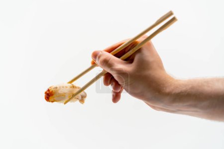 Foto de Primer plano de la mano de un hombre con palillos que sostienen un sushi de anguila en el aire sobre fondo blanco - Imagen libre de derechos
