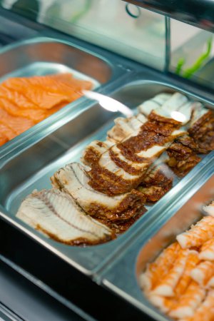 Foto de Primer plano de ingredientes de sushi en bandejas profesionales de metal salmón camarones anguila camarones aguacate en la cocina del restaurante de sushi - Imagen libre de derechos