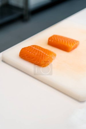 Téléchargez les photos : Gros plan d'un filet de saumon couché sur un tableau de cuisine blanc dans la cuisine du restaurant de sushi - en image libre de droit