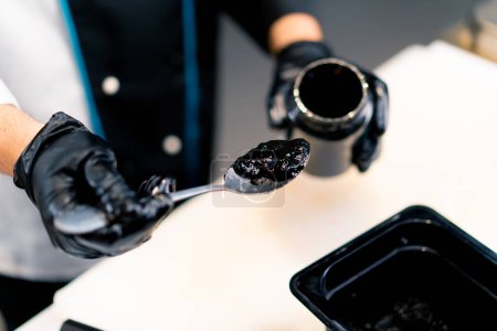 Photo for Close-up of a sushi chef pulling cuttlefish ink out of a jar with a spoon to make black rice at a sushi restaurant - Royalty Free Image