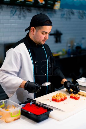Foto de Primer plano de un chef de sushi decorando rollo con atún y queso de camarón antes de hornear en el proceso de sushi al horno - Imagen libre de derechos