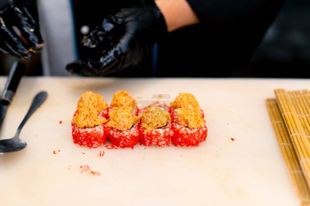 Téléchargez les photos : Gros plan d'un chef sushi décorant un rouleau de thon et de fromage aux crevettes avant la cuisson au four - en image libre de droit