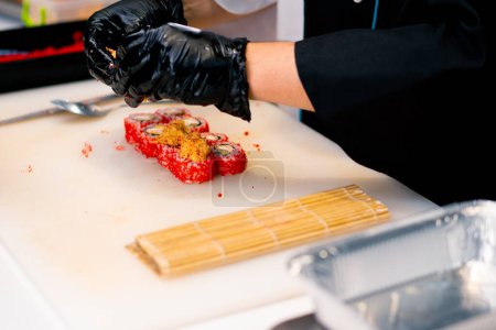 Téléchargez les photos : Gros plan d'un chef sushi décorant un rouleau de thon et de fromage aux crevettes avant la cuisson au four - en image libre de droit