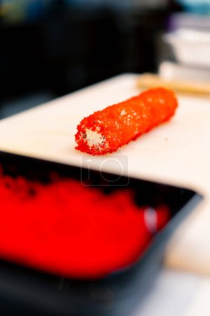 Téléchargez les photos : Gros plan sushi chef décorer un rouleau de thon et de crevettes avec du caviar tobiko avant de cuire au four dans le processus de sushi cuit au four - en image libre de droit
