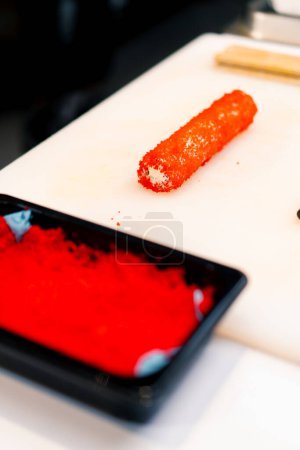 Photo for Close-up sushi chef decorating a tuna and shrimp roll with tobiko caviar before baking in the oven baked sushi process - Royalty Free Image