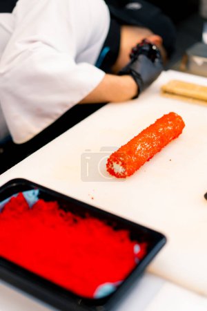 Foto de Primer plano chef de sushi decorando un rollo de atún y camarones con caviar tobiko antes de hornear en el proceso de sushi al horno - Imagen libre de derechos