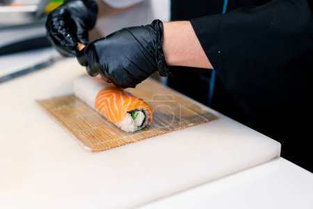 Foto de Chef de sushi en el proceso de preparación de rollo de Filadelfia con camarones de queso crema de salmón y algas chuka en una estera de sushi de bambú - Imagen libre de derechos