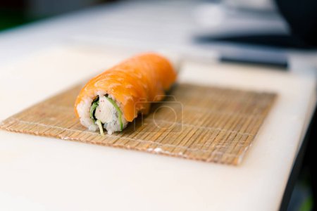 Foto de Un primer plano de un chef de sushi envolviendo un rollo de filipina en salmón usando estera de sushi de bambú en la mesa de la cocina - Imagen libre de derechos