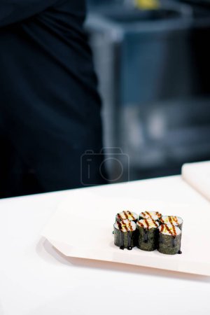 Photo for A close-up of maki rolls with avocado that the sushi chef is pouring unagi sauce on the kitchen table in the kitchen of sushi restaurant - Royalty Free Image