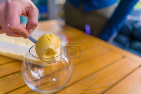 Photo for Close-up of a waiter in a cafe taking a scoop of ice cream with an ice cream spoon and putting it into glass - Royalty Free Image