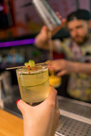 Foto de El cliente sostiene delicioso cóctel de jardín de ginebra recién hecho con pepino en el concepto de bebidas bar bar de mano - Imagen libre de derechos