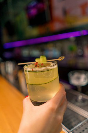 Photo for Customer holding delicious freshly made gin garden cocktail with cucumber in hand bar bar drinks concept - Royalty Free Image