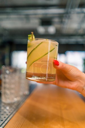 Foto de El cliente sostiene delicioso cóctel de jardín de ginebra recién hecho con pepino en el concepto de bebidas bar bar de mano - Imagen libre de derechos