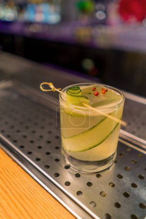 Foto de Recién preparado gin garden cóctel alcohólico con rodajas de pepino se encuentra en el mostrador de bar en el bar club - Imagen libre de derechos