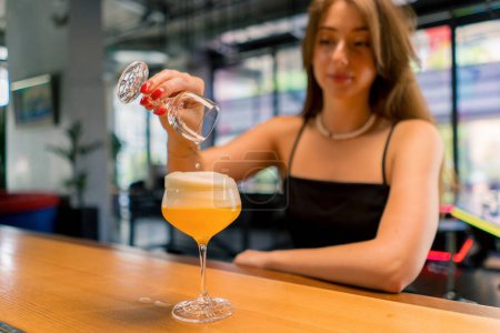 Téléchargez les photos : Fille souriante au bar verser de l'eau d'un verre dans un cocktail alcoolisé le concept de boissons dans le club - en image libre de droit