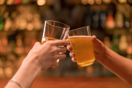 Photo for Close up of a couple of guys and a girl toast with glasses of beer at the bar in club bar - Royalty Free Image