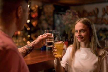 Photo for A young smiling girl with a glass of beer in her hand is chatting with a man at the bar in club bar - Royalty Free Image