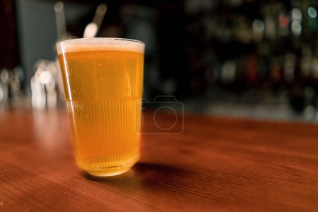 Photo for Close up of a glass of beer on a wooden bar counter in club bar the concept of love for beer and alcoholic beverages - Royalty Free Image
