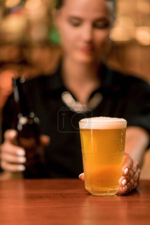 Téléchargez les photos : Gros plan d'une serveuse versant de la bière d'une bouteille dans un verre au bar du club bar - en image libre de droit