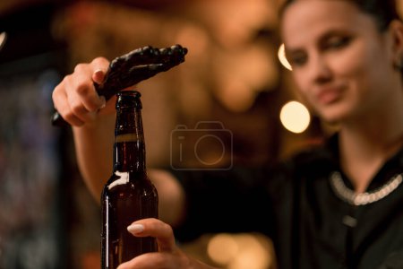 Photo for Close up of a female bartender opening a closed glass bottle of beer on the bar in club bar - Royalty Free Image