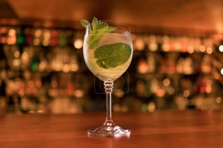 Photo for Close-up of a cocktail with ice and mint next to the bar against the background of alcoholic drinks in club bar - Royalty Free Image