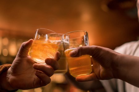 Téléchargez les photos : Gros plan d'un groupe de trois amis debout au bar discutant et trinquant avec des verres de bière et un cocktail au bar du club - en image libre de droit