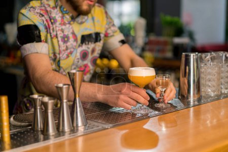 Téléchargez les photos : Un jeune barman professionnel donne un délicieux cocktail alcoolisé au client en club au bar - en image libre de droit