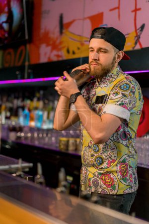 Téléchargez les photos : Jeune barman professionnel mélangeant de l'alcool dans un shaker en métal. Le processus de fabrication de cocktails en club dans un bar - en image libre de droit