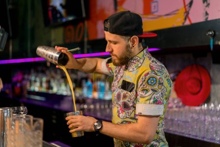 Foto de Cantinero joven profesional mezclando alcohol en una coctelera de metal. El proceso de hacer cócteles en el club en un bar - Imagen libre de derechos