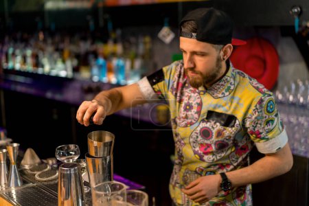 Téléchargez les photos : Jeune barman professionnel verse de l'alcool d'une tasse à mesurer dans un shaker Processus de fabrication de cocktails dans un club dans un bar - en image libre de droit