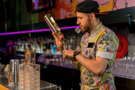 Téléchargez les photos : Un jeune barman professionnel verse de l'alcool dans une tasse à mesurer Le processus de fabrication de cocktails en club dans un bar - en image libre de droit
