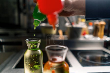 Foto de Un chef en experimentos profesionales de cocina añadiendo granos de caviar molecular multicolor a un recipiente con agua de cerca - Imagen libre de derechos