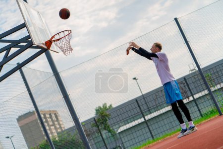 Photo for Tall guy basketball player throws a ball into a basketball hoop at a basketball court in the park during practice - Royalty Free Image