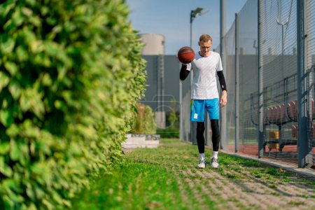 Téléchargez les photos : Grand joueur de basket-ball gars marche sur le chemin du parc pour le terrain de basket-ball et conduit la balle montrant ses compétences dribble - en image libre de droit