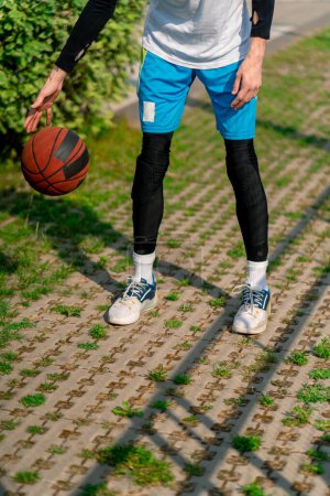 Foto de Alto jugador de baloncesto chico camina por el camino del parque a la cancha de baloncesto y conduce la pelota mostrando sus habilidades de goteo de cerca - Imagen libre de derechos