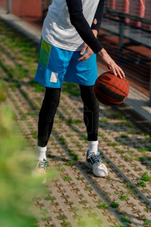 Photo for Tall guy basketball player walks down the park path to the basketball court and drives the ball showing off his dribbling skills close-up - Royalty Free Image