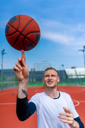 Téléchargez les photos : Gros plan d'un joueur de basket-ball filant un ballon de basket-ball sur son doigt montrant ses compétences en style libre de basket-ball - en image libre de droit