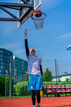 Téléchargez les photos : Grand joueur de basket-ball saute au cerceau avec la balle à la main pour marquer un dunk spectaculaire pendant l'entraînement sur le terrain de basket dans le parc - en image libre de droit