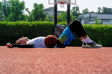 Photo for Tall guy basketball player lying on a basketball court in the park along with  basketball resting during practice - Royalty Free Image