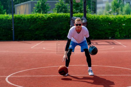 Foto de Un jugador de baloncesto de hombre alto con dos bolas muestra sus habilidades de driblar mientras practica en la cancha de baloncesto en el parque - Imagen libre de derechos
