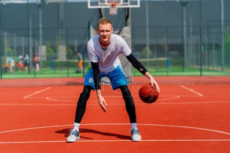 Photo for Tall guy basketball player with the ball shows his dribbling skills during practice on the basketball court in the park - Royalty Free Image