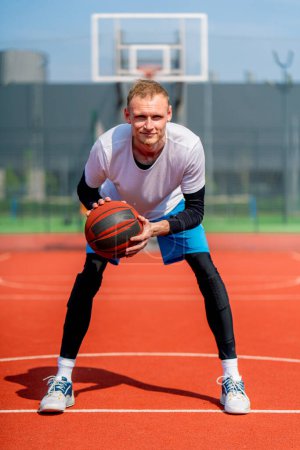 Photo for Portrait of a tall guy basketball player holding a ball in his hands on a basketball court in park - Royalty Free Image