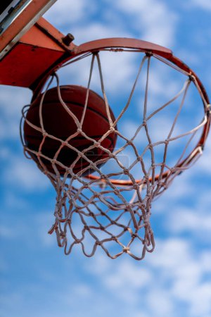 Téléchargez les photos : Un gros plan de basket-ball cerceau dans lequel un basket-ball frappe le concept de l'admiration pour le jeu de basket-ball et l'amour de travailler - en image libre de droit
